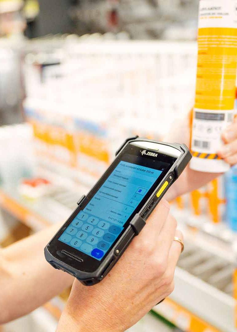 Hand houdt handscanner vast en scant label van product met winkelstelling op de achtergrond.