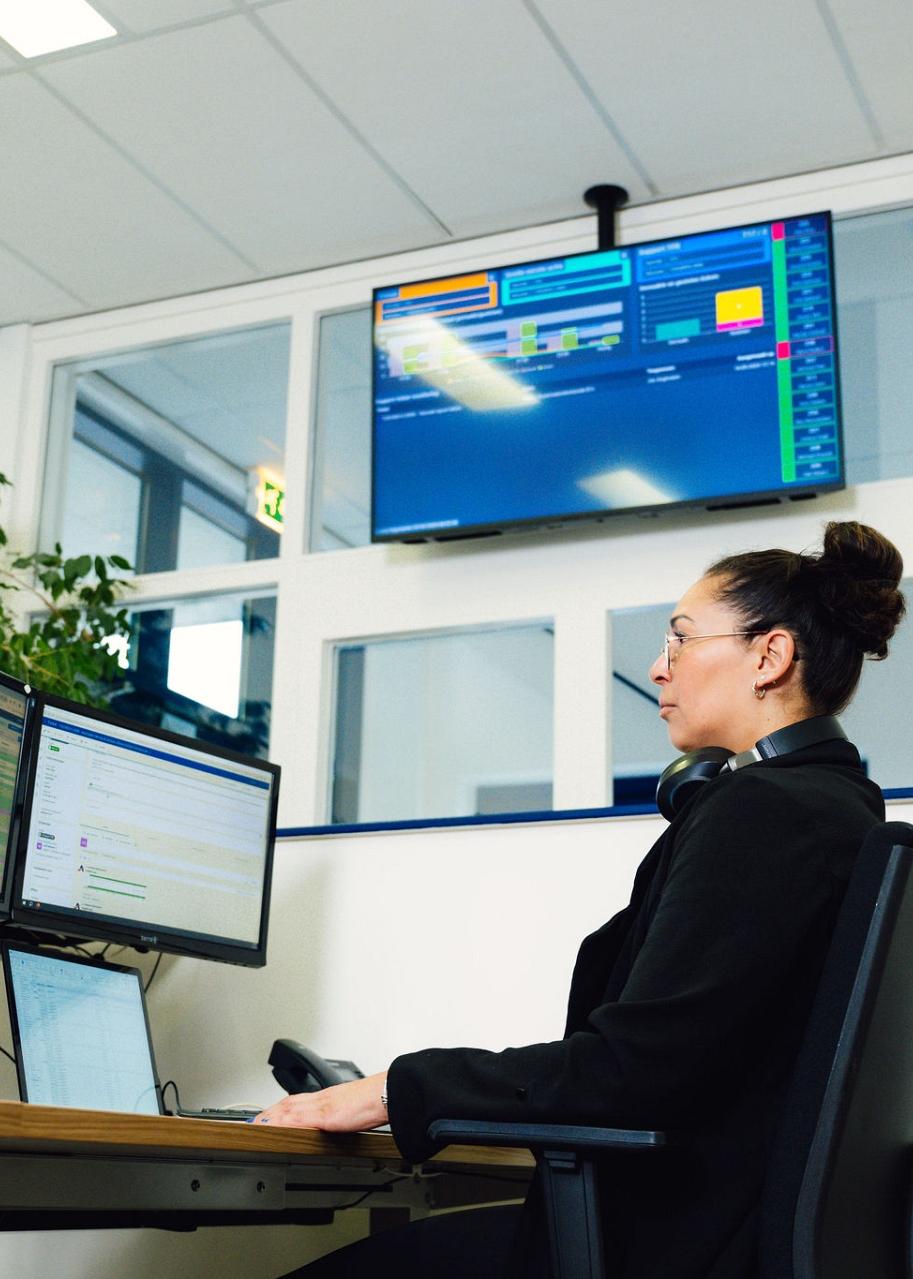Een vrouw aan een werkstation met meerdere monitoren die verschillende gegevens en grafieken weergeven, in een professionele omgeving.