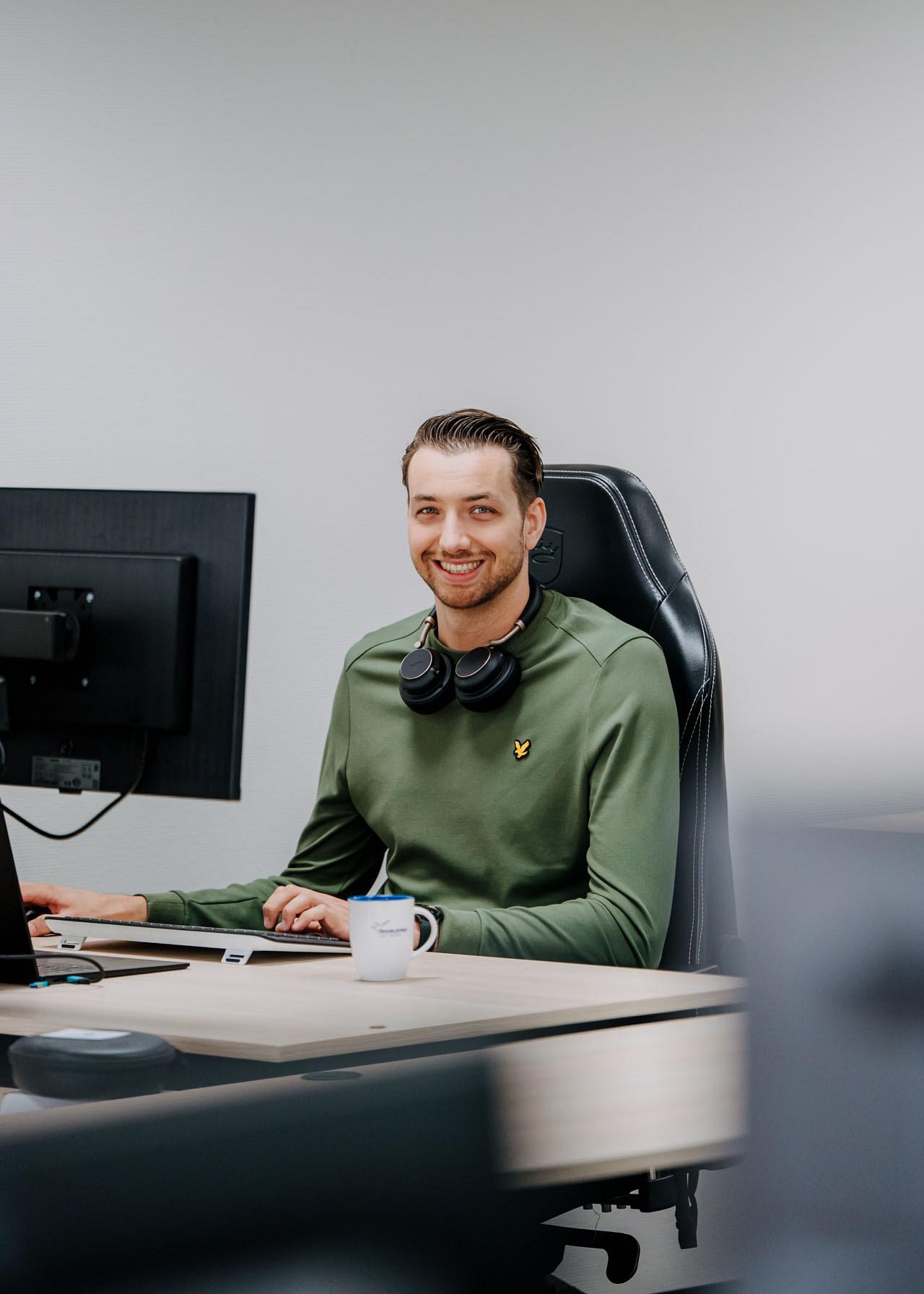 Supportmedewerker werkt achter computer met headset op kantoor en kijkt glimlachend richting camera