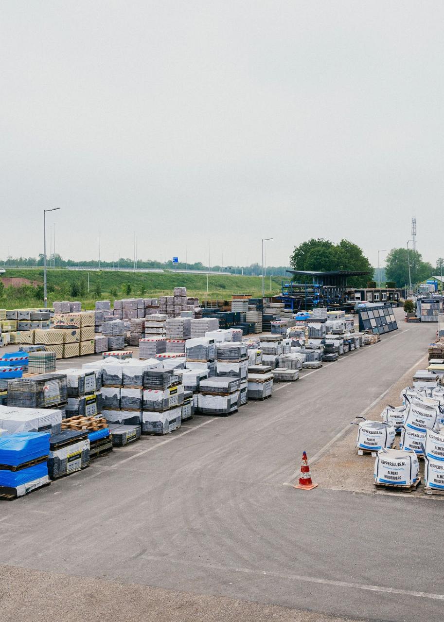 Overzicht van bedrijfsterrein met bouwmateriaal in zakken en op pallets.
