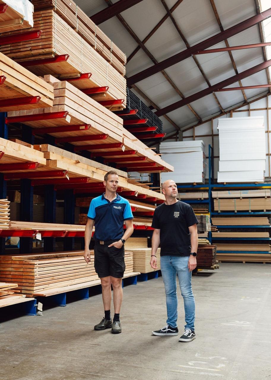 2 mannen staan in een grote hal voor een stelling vol houten balken.