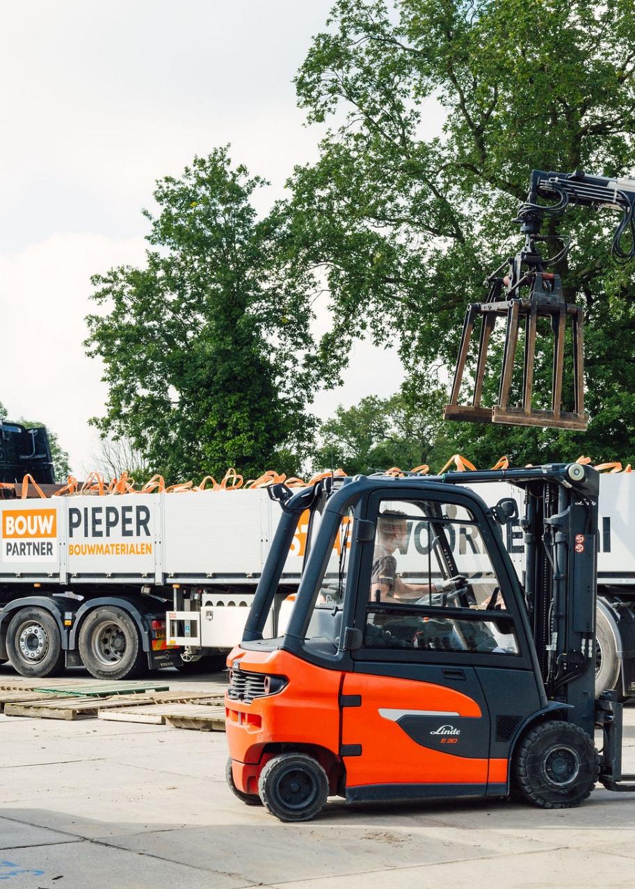 Heftruck voor een vrachtwagen met grijper die lading inlaadt op een bedrijventerrein.