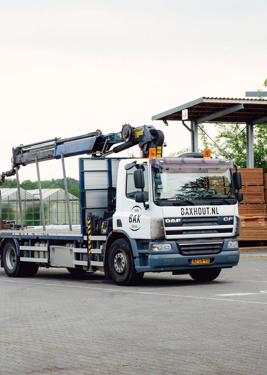 Vrachtwagen en heftruck met op de achtergrond grote pallets met hout.