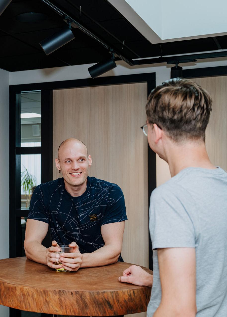 Twee collega’s in gesprek bij een statafel in het kantoor van Smart Trade en Smart Bulb, met beide logo’s zichtbaar op de muur.