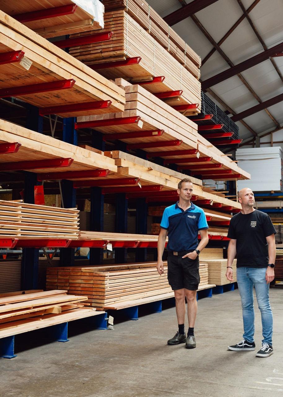 2 mannen staan in een grote hal voor een stelling vol houten balken.