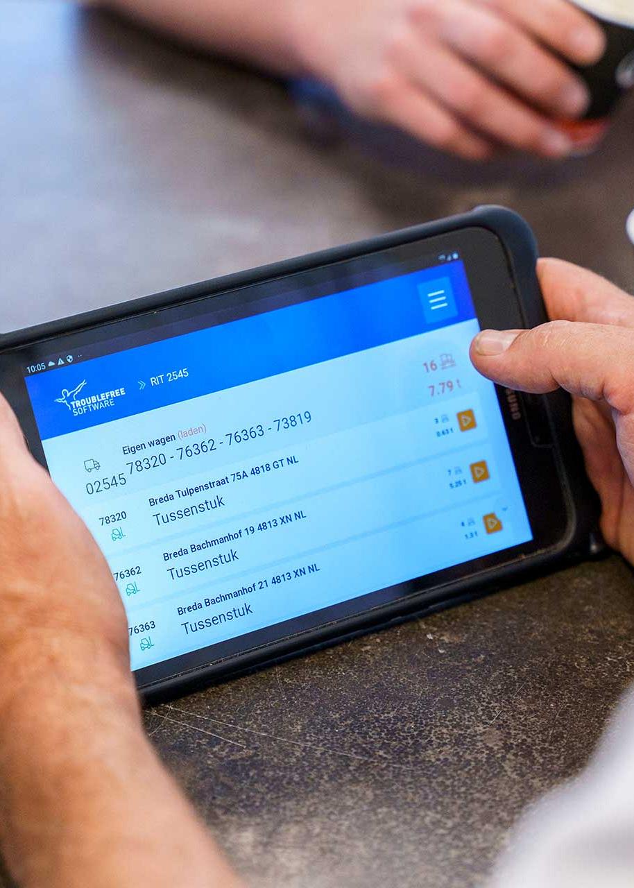 Handen die tablet vasthouden met Troublefree software, met op de achtergrond een gouden bel en een kartonnen beker.