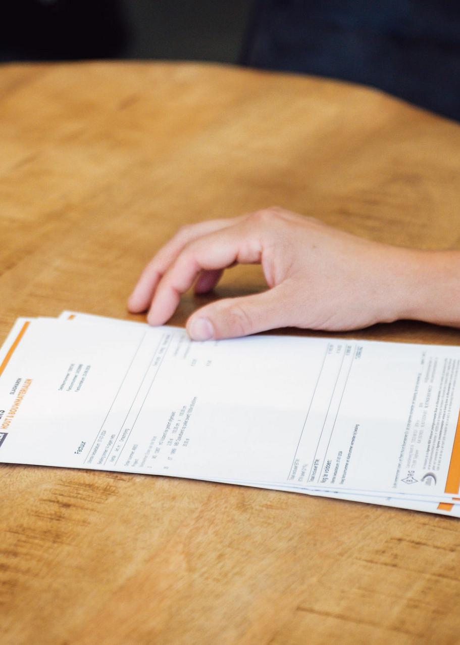 Een arm naast papieren met informatie liggen op een ronde houten tafel.