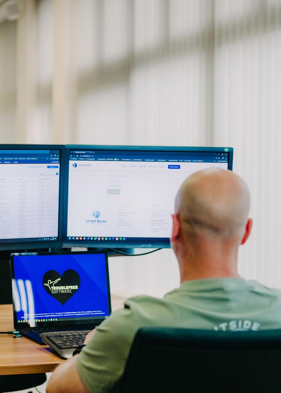 Man aan bureau met 2 monitoren en een laptop voor zich.