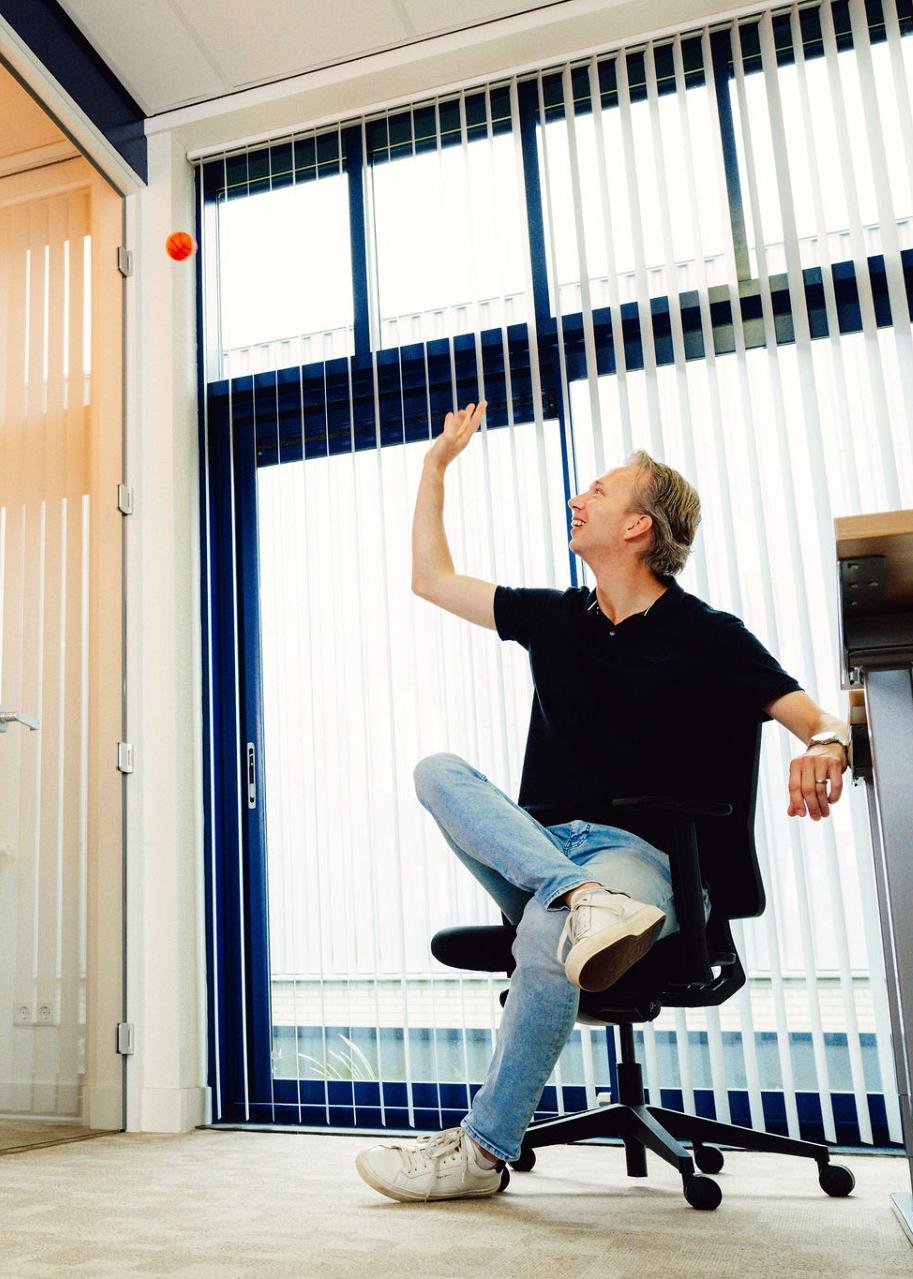 Man die zit in een stoel aan bureau terwijl hij een balletje naar een net gooit. 