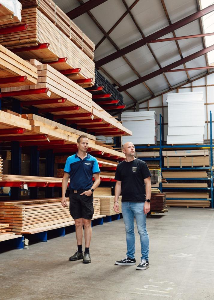 2 mannen staan in een grote hal voor een stelling vol houten balken.
