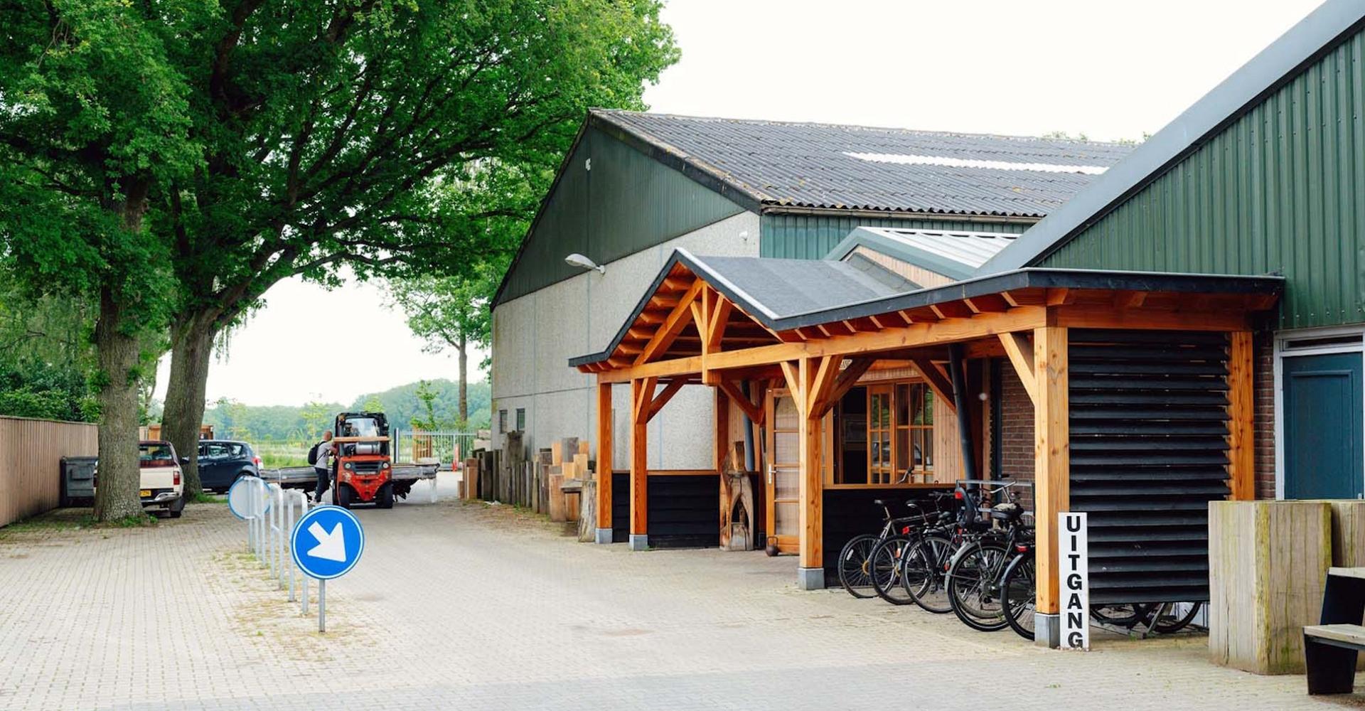 Voorkant van bedrijvenpand met houten voorgevel, fietsenstalling en op de achtergrond een heftruck.