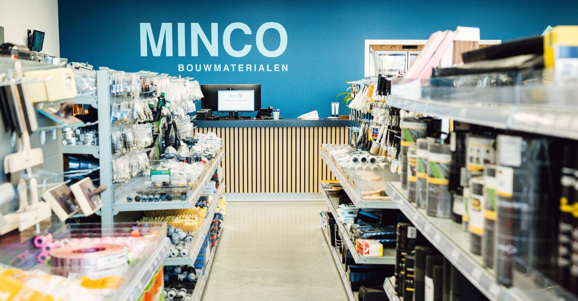 Een gangpad in een bouwmaterialen, met een blauwe want met Minco logo op de achtergrond.