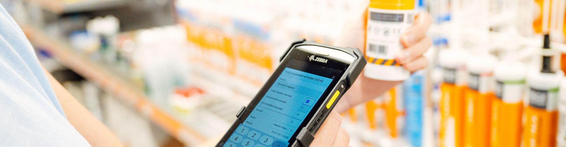 Hand houdt handscanner vast en scant label van product met winkelstelling op de achtergrond.