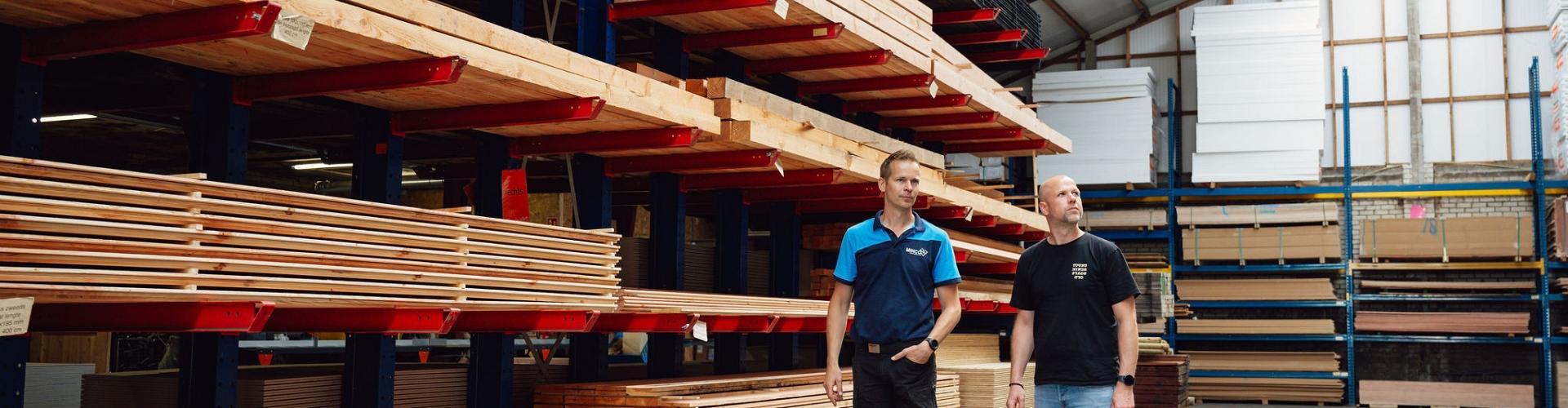 2 mannen staan in een grote hal voor een stelling vol houten balken.