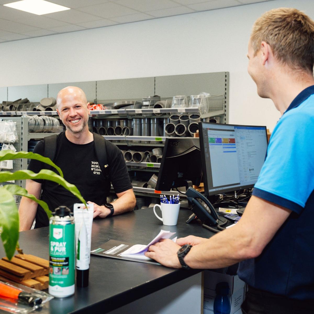 Man achter balie met op computer Smart Trade software met een lachende man.