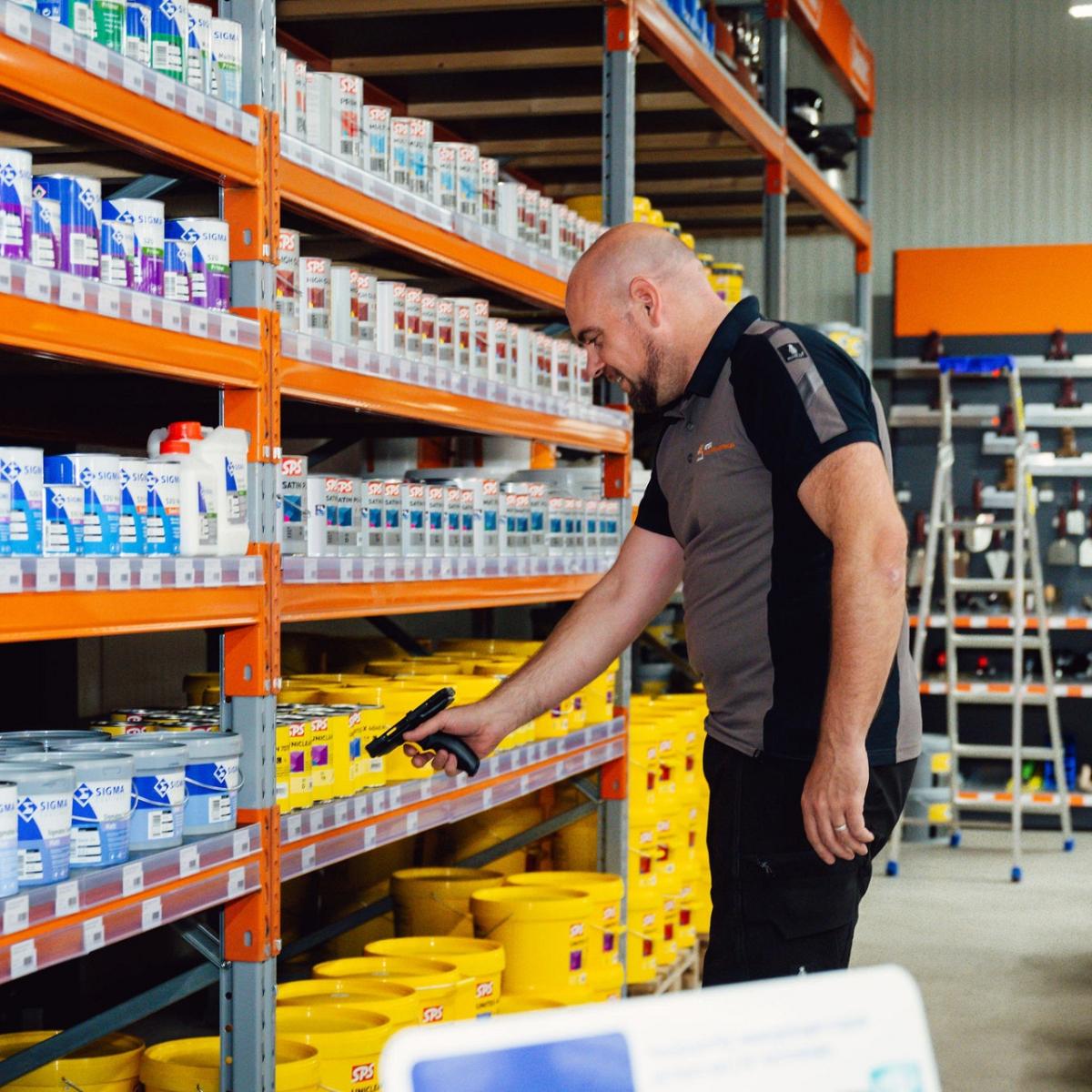 Man scant een product in een schap met verschillende verfblikken en emmers.