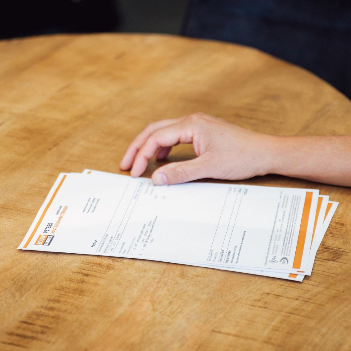 Stapeltje van papieren op een tafel met een hand ernaast.