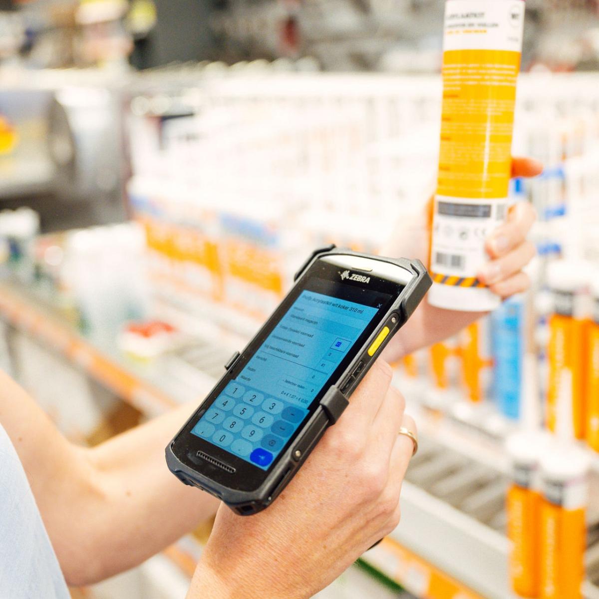 Persoon scant een koker afdichtmiddel met een mobiele scanner in een winkel, met schappen vol vergelijkbare producten op de achtergrond.