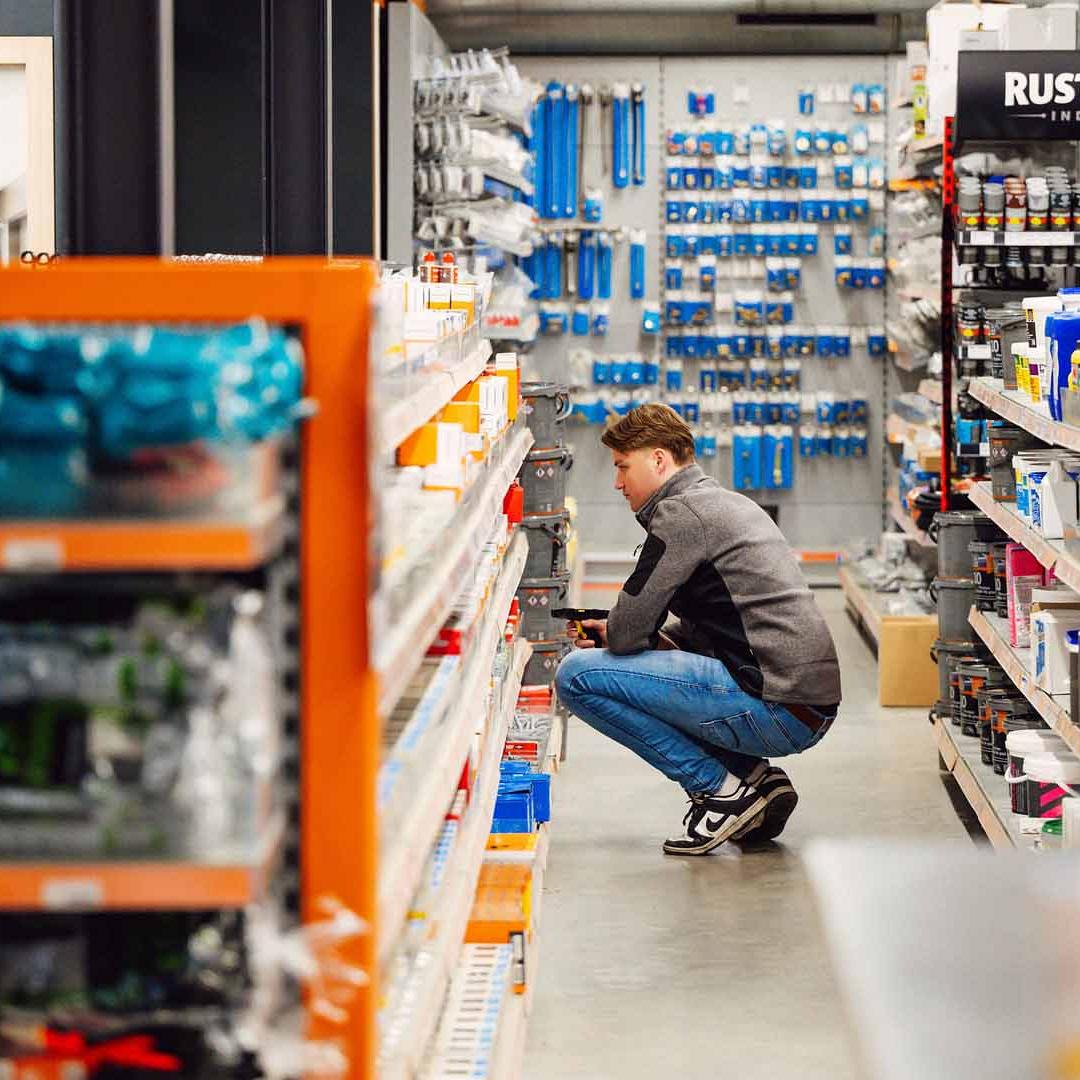 Man bukt bij schap om product te scannen met handscanner in een winkelomgeving.