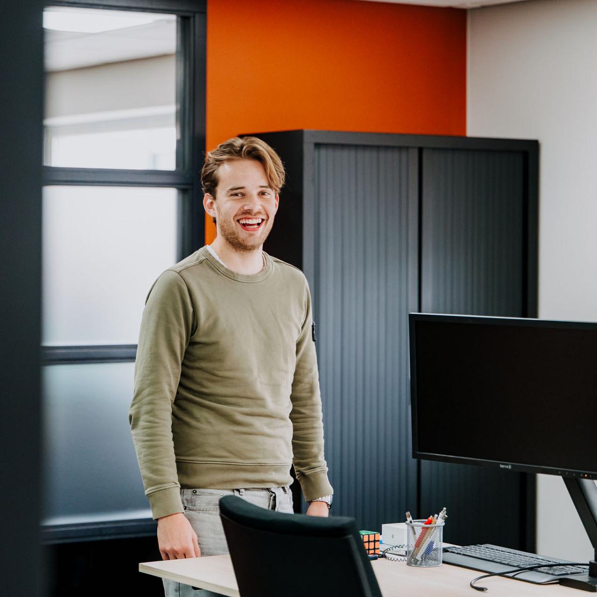 Medewerker staat lachend bij bureau met computer op kantoor