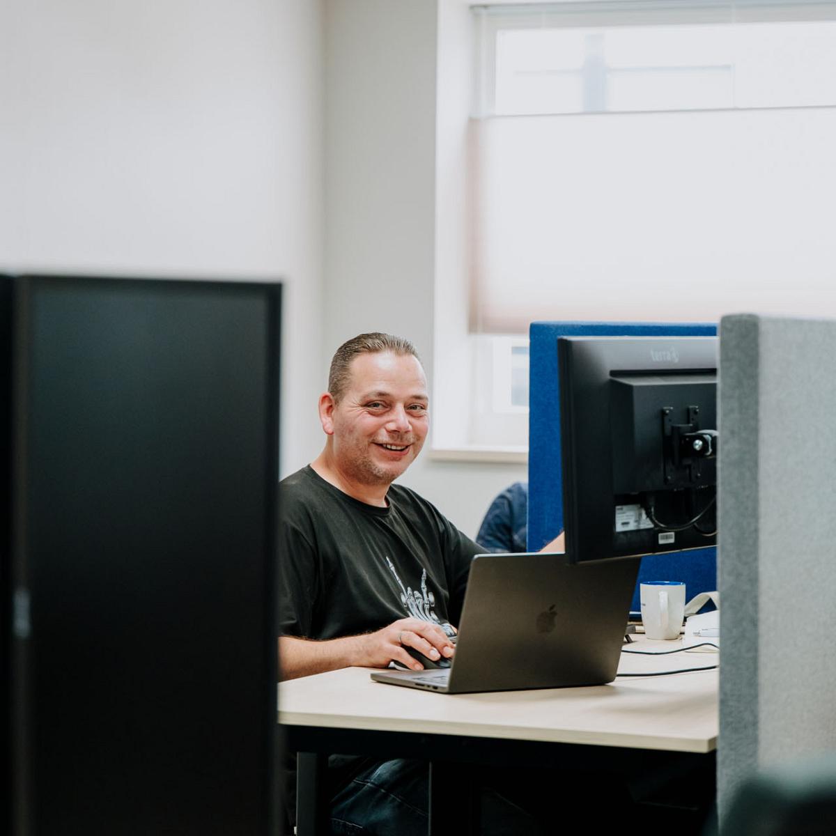 Supportmedewerker werkt achter laptop op kantoor en kijkt glimlachend