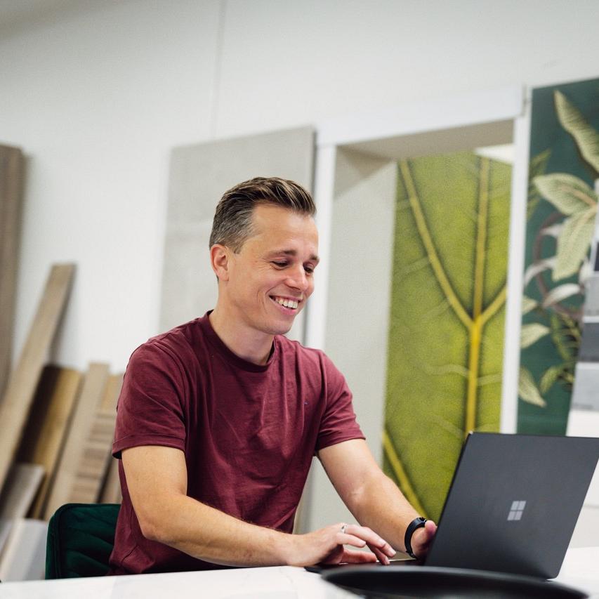 Man zit achter bureau met laptop voor zich waarop hij kijkt al glimlachend in een winkelomgeving.