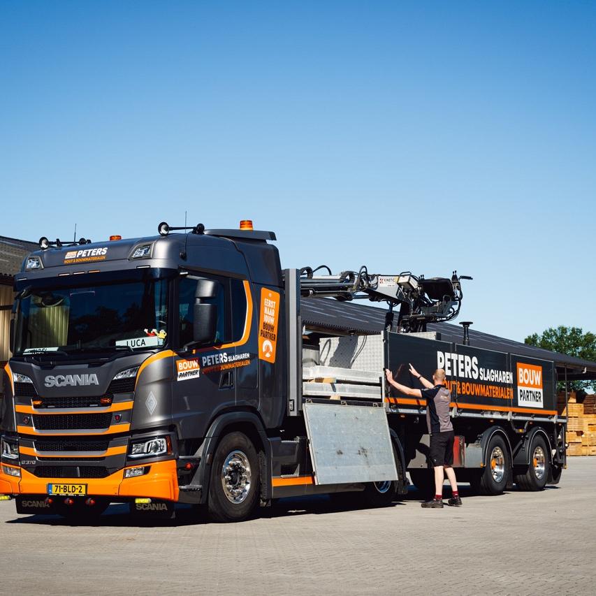 Oranje/ zwarte vrachtwagen die gelost wordt door man.