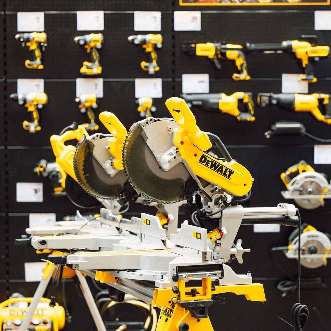 Een wand vol gele DeWalt-gereedschappen, met op de voorgrond twee cirkelzagen op een montagetafel.