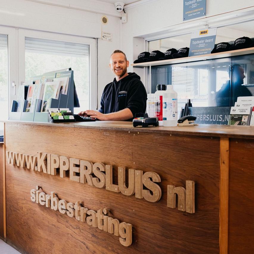 Man achter een balie met allemaal flyers die op zijn computer zit terwijl hij lacht.