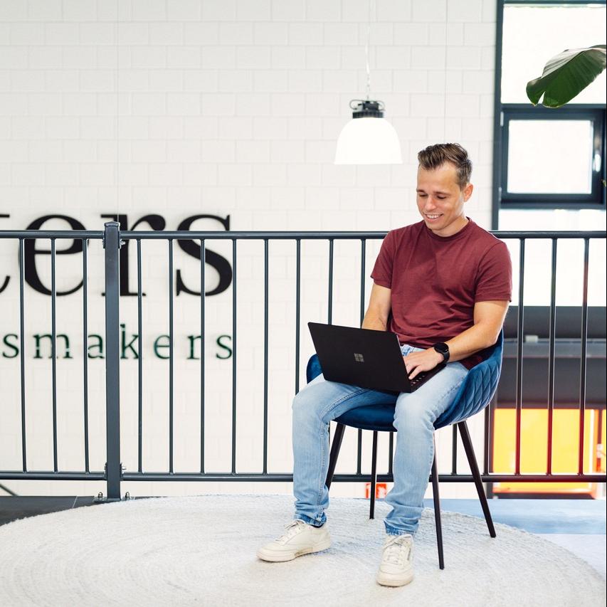 Man werkt op zijn laptop op een stoel met op de achtergrond een traphek.