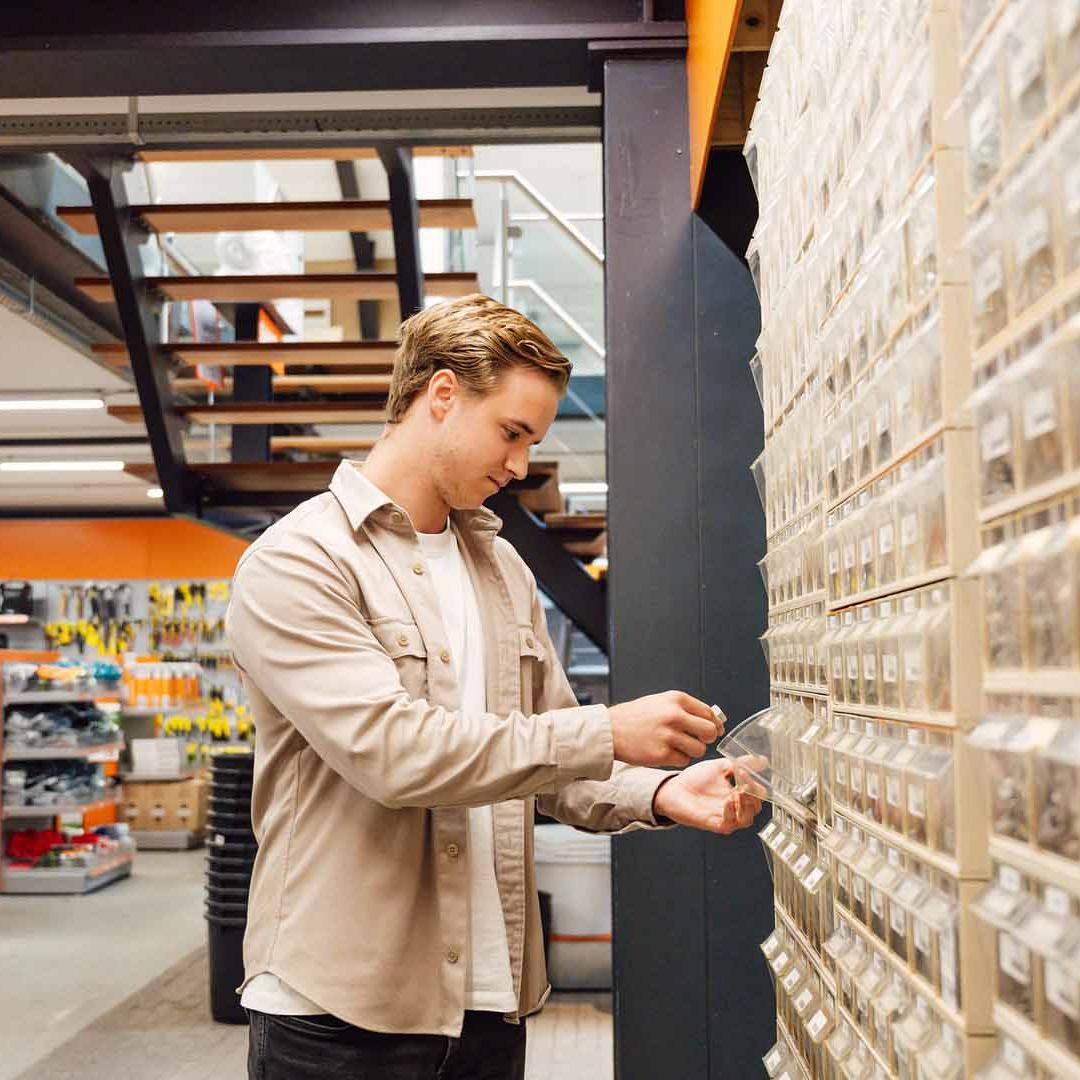Man staat bij wand met doorzichtige opbergbakjes en pakt er iets uit met een winkelomgeving op de achtergrond.