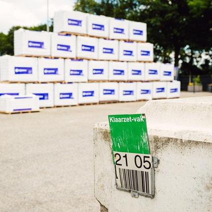 Stapel witte isolatiepanelen van Recticel in een opslagplaats, gemarkeerd met een groene kaart 'Klaarzet-vak' en barcode 2105.