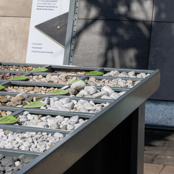 Vakken met siergrind en keien in verschillende kleuren en formaten, met tegelpanelen op de achtergrond.