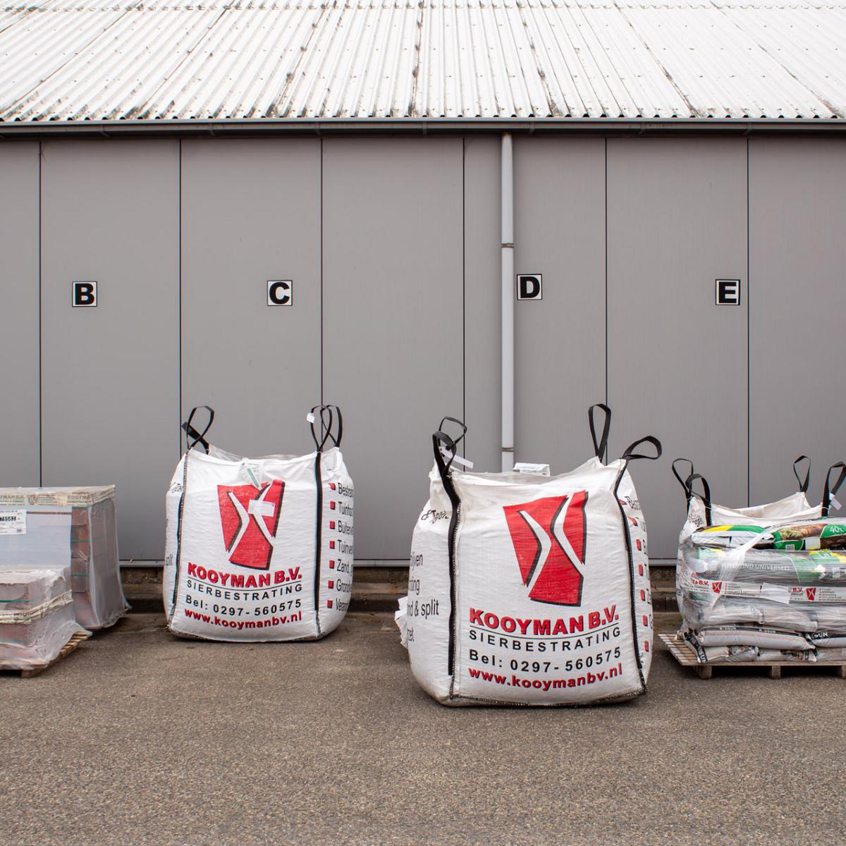 Big bags en pallets met sierbestrating en tuinmaterialen op het buitenterrein van Kooyman B.V.