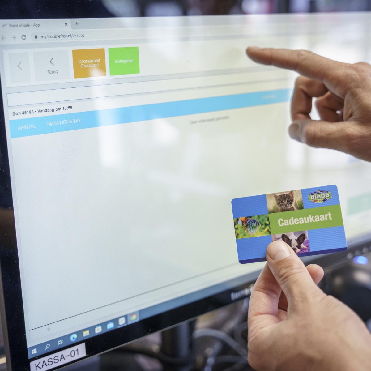 Hand wijst naar computerscherm met webpagina en cadeaukaart in andere hand.