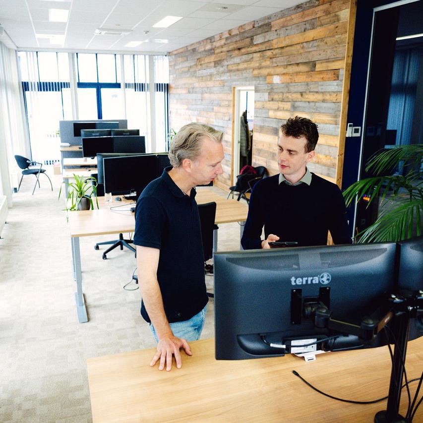 Twee mannen staan aan het bureau met twee geschakelde monitors en praten met elkaar.