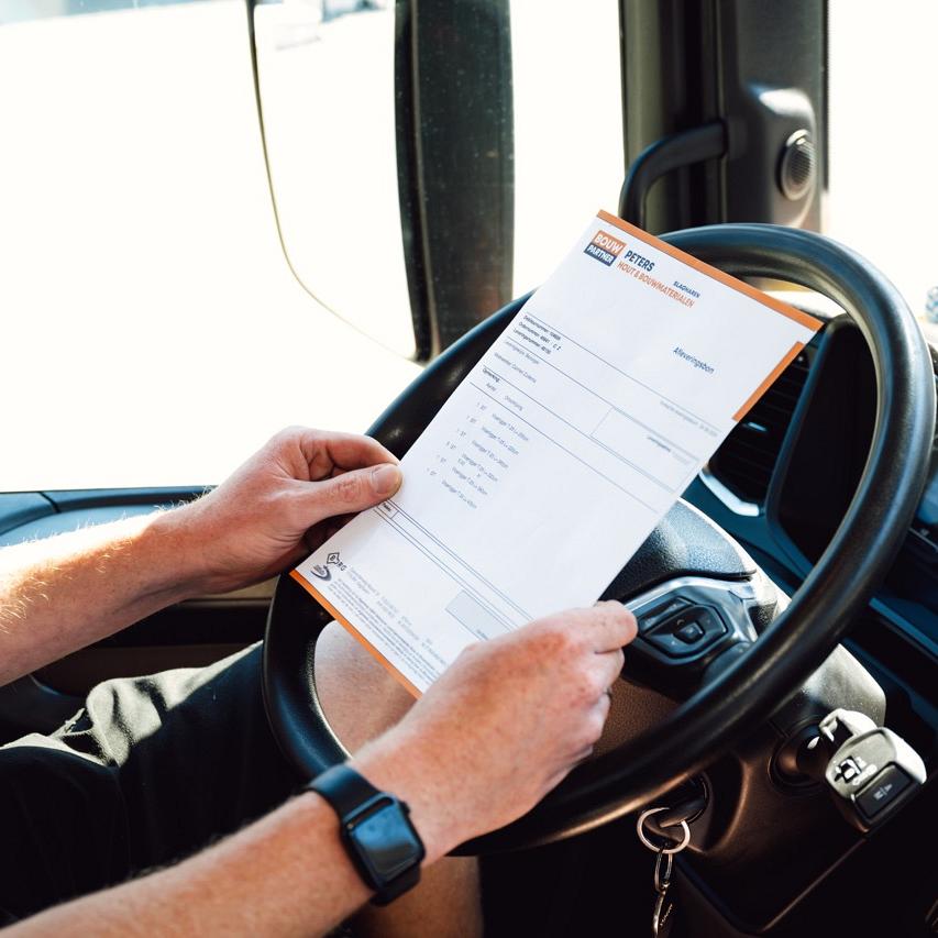 Persoon houdt papier vast bovenop autostuur in een auto.