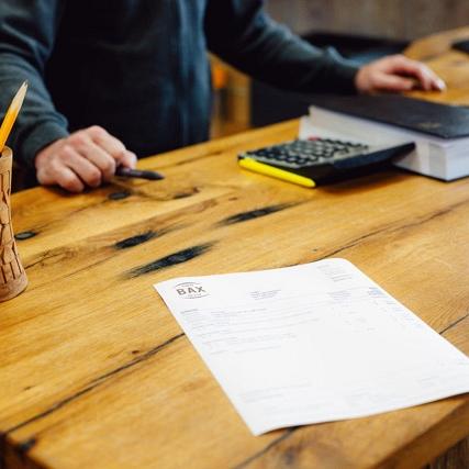 Houten bureau met kantoorspullen erop en een persoon die erachter staat.