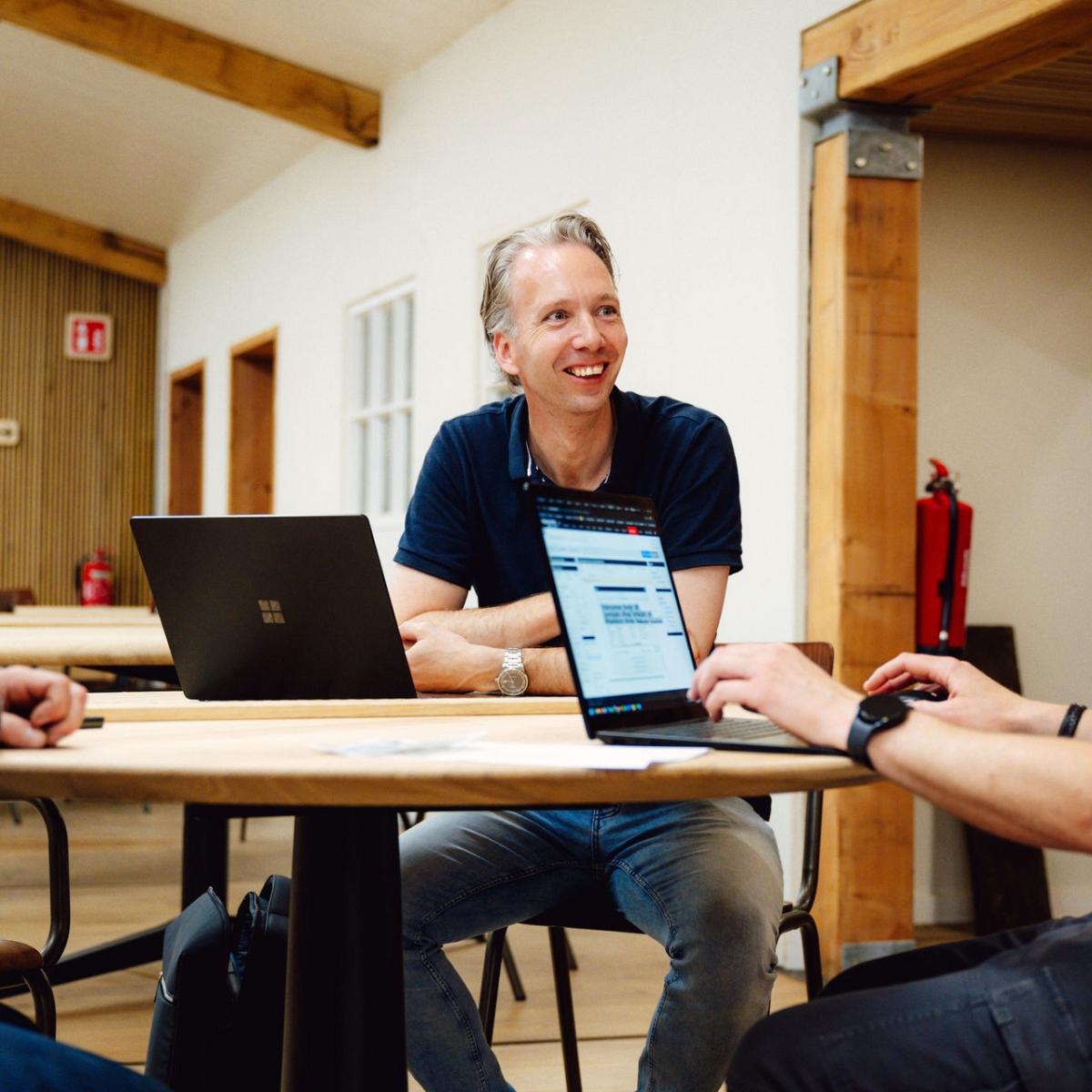 Twee mannen aan een tafel die aan het werk zijn op eigen laptops.