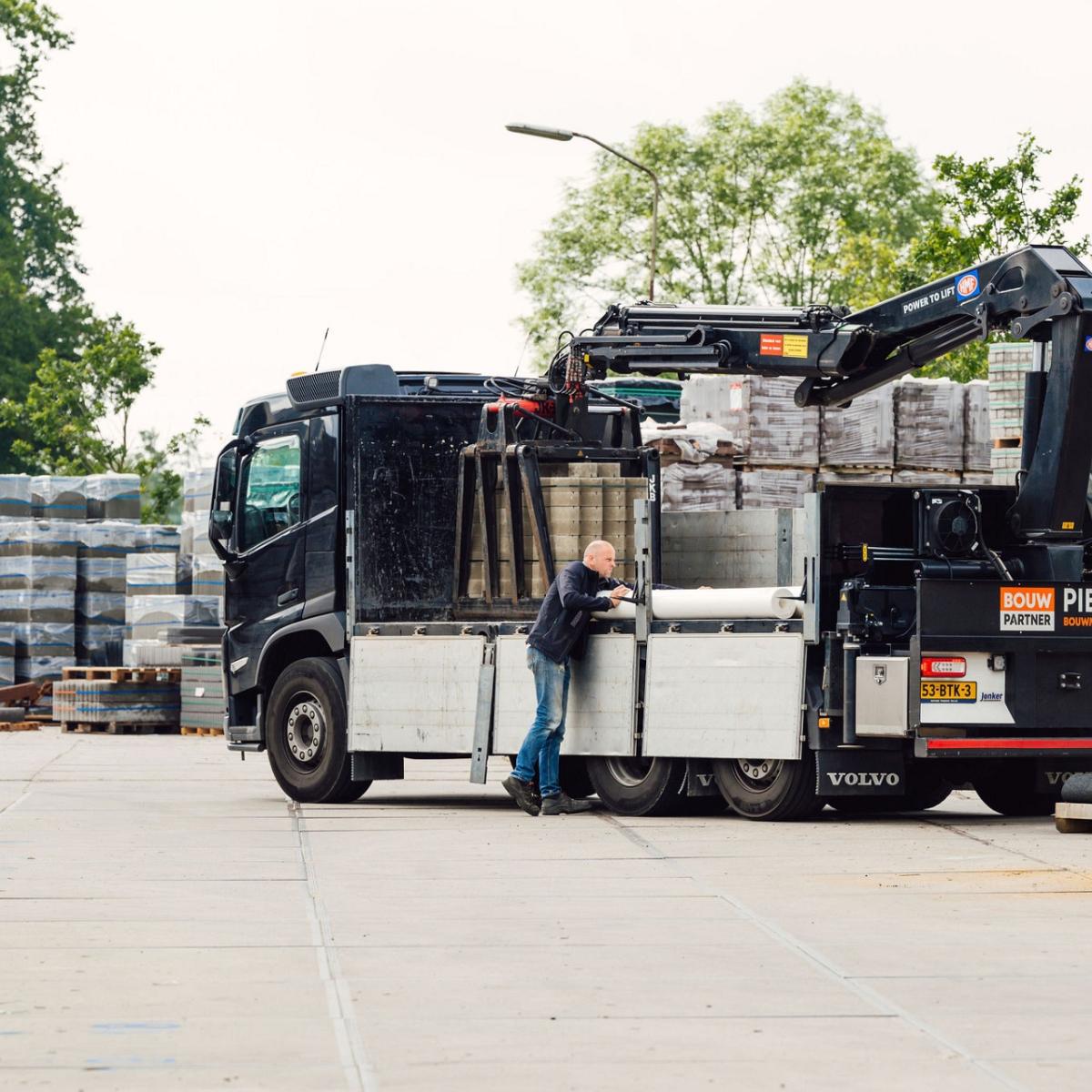 Achterkant van vrachtwagen die gelost wordt door man die aan de voorzijde staat.