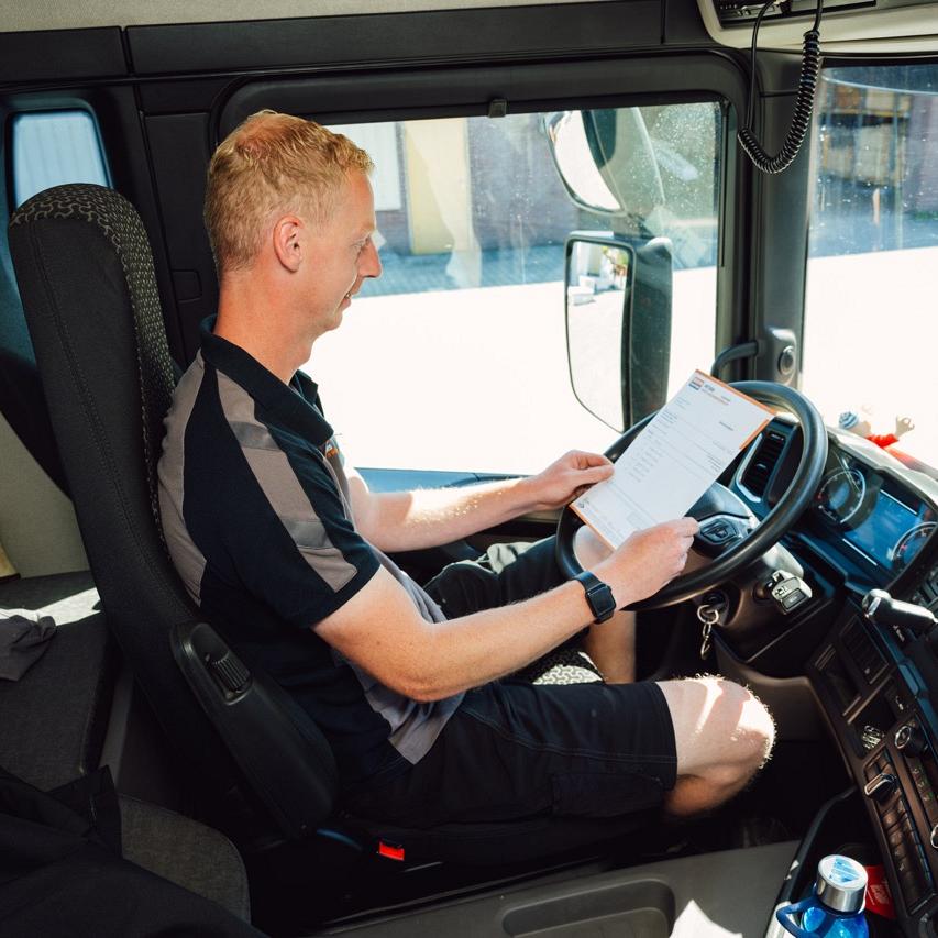  Man die achter het stuur zit van een vrachtwagen met een formulier in zijn handen waar hij naar kijkt.