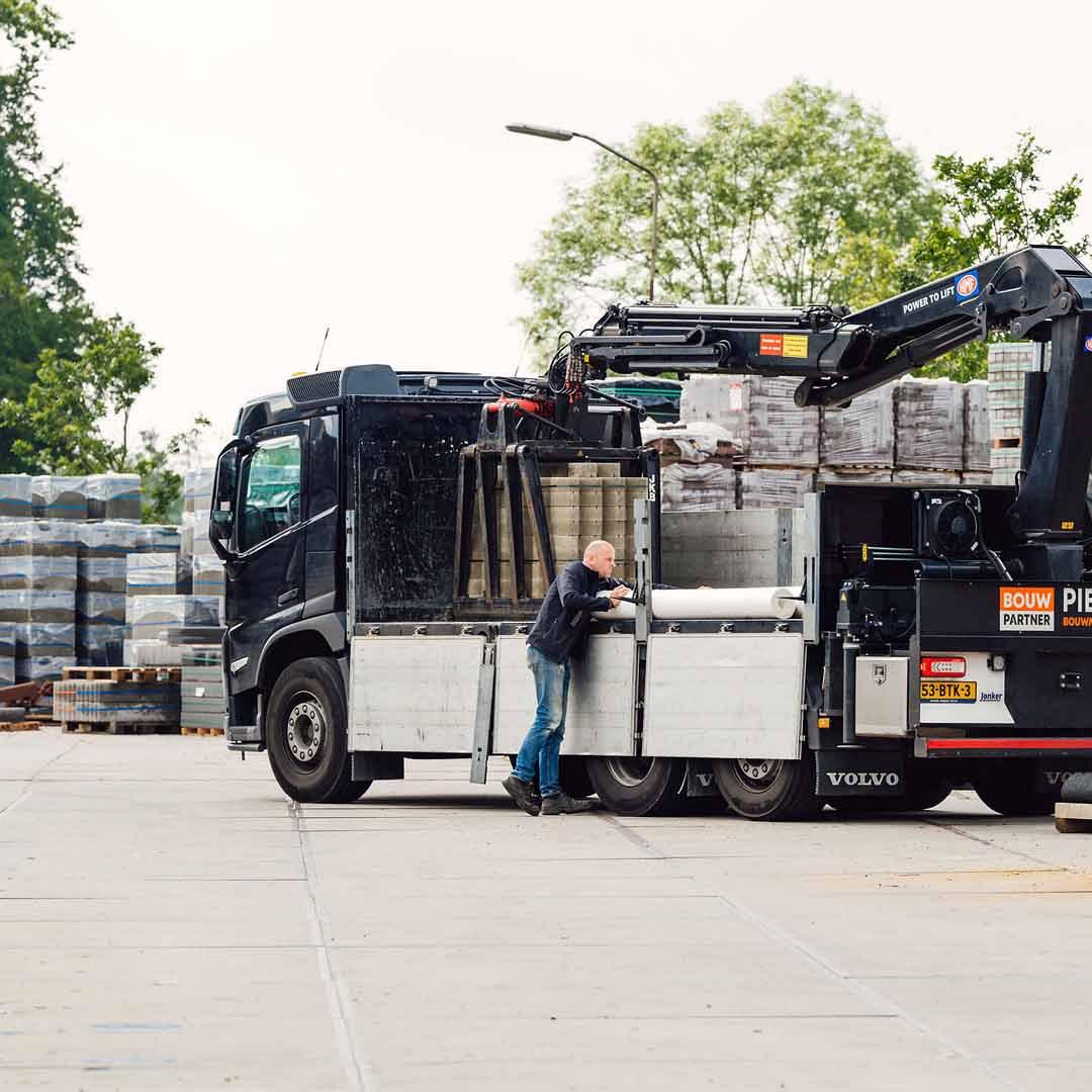 Achterkant van vrachtwagen die gelost wordt door man die aan de voorzijde staat.