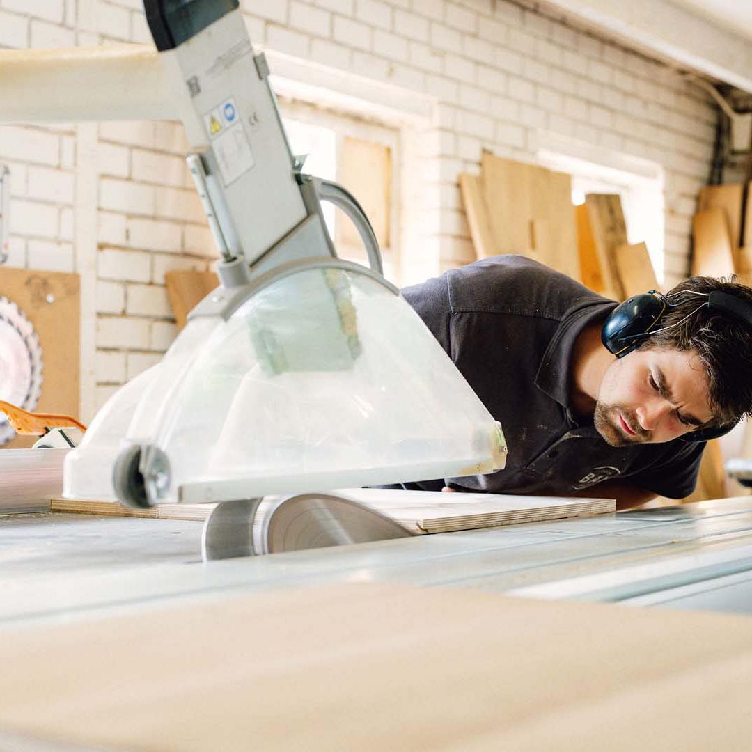 Man met gehoorbescherming op die geconcentreerd kijkt naar een grote cirkelzaag.