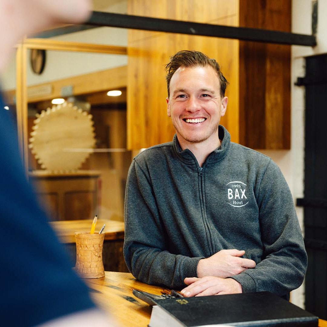 Lachende man die aan een tafel staat met op de tafel en pennenbak en agenda en op de achterkant is een deur met ‘opslag’ erop.