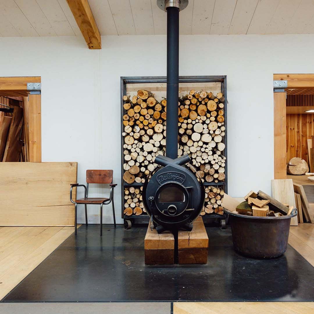 Houtoven met op de achtergrond stelling met verschillende ronde houten stammen en naast de oven een emmer met houtblokken.