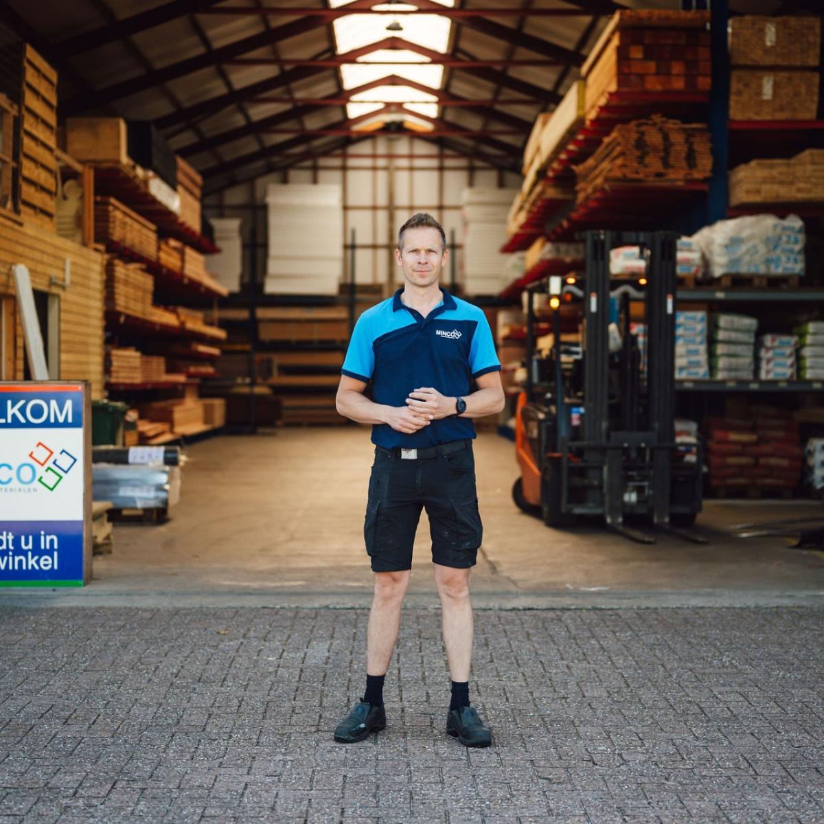 Persoon voor de ingang van een grote hal met handen ineengeslagen.