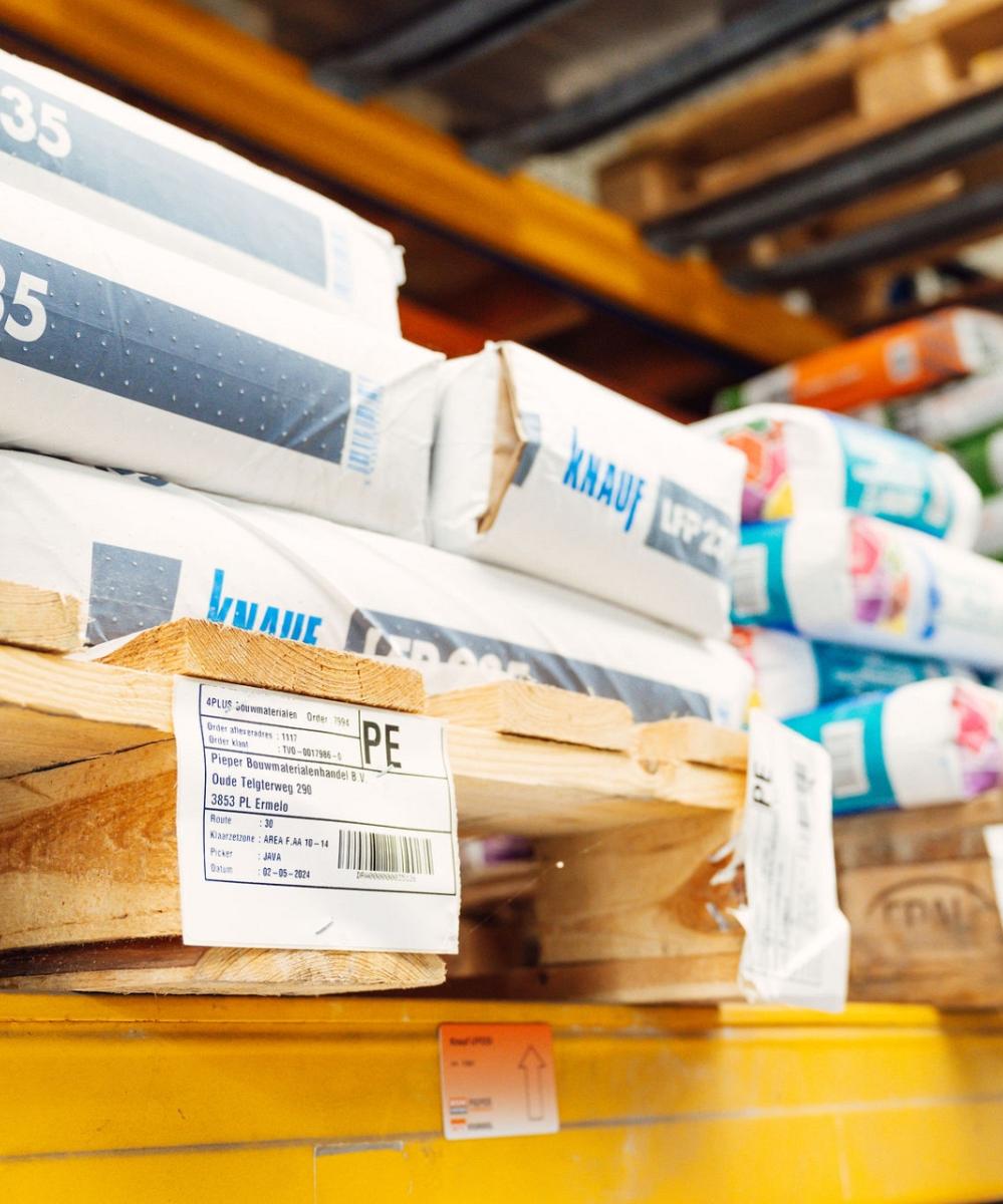 Close-up van houten pallets met daarop gestapelde bouwmaterialen, waaronder verpakkingen van Knauf LFP 235, voorzien van labels met productinformatie.