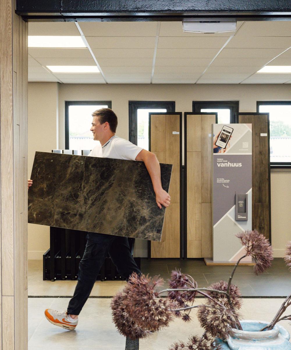 Displaywand met een uitgebreid assortiment tegel- en plaatmateriaal in diverse kleuren, structuren en afwerkingen, overzichtelijk gepresenteerd in een showroom.