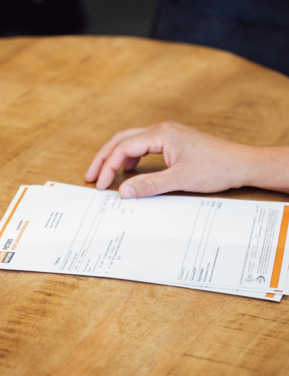 Stapeltje van papieren op een tafel met een hand ernaast.