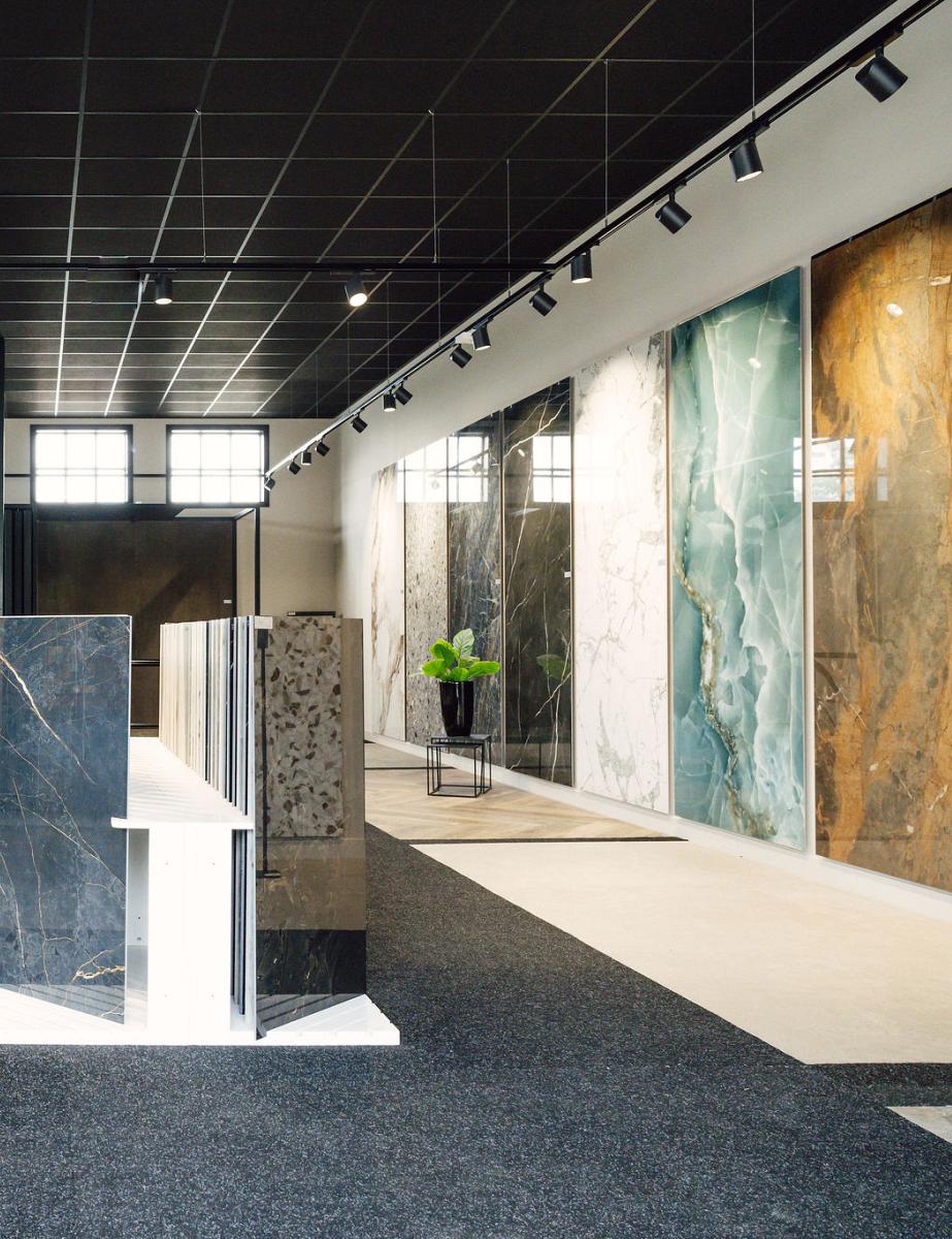 Ruime en modern ingerichte showroom met grote wand- en vloertegels in diverse kleuren en patronen, overzichtelijk gepresenteerd in een strak verlichte ruimte.